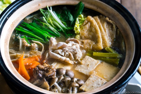 A Japanese earthenware pot (Donabe) containing vegetables, tofu, and pork cooked in sesame and miso based soup broth.
